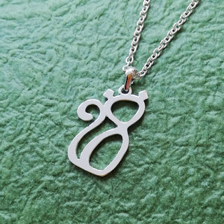 Silver color cat necklace designed with Arabic word on green paper. Sitting up posture, the chain is connected to its head.