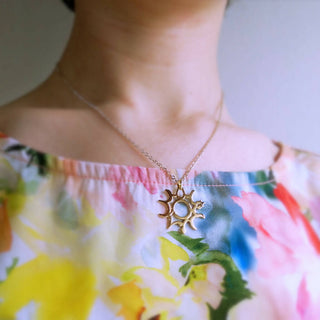 A model is wearing gold sun motif necklace on floral pattern top.