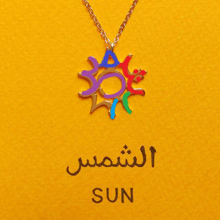 Gold sun motif necklace on orange card with an Arabic word.