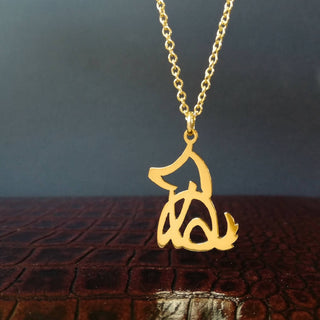 Gold dog motif necklace hanging down. The sitting shape is designed with Japanese word that means dog. The pendant top is flat, cutout and shiny, facing left. The chain is attached to its ear.