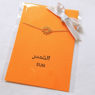 Wrapping sample photo of gold sun bracelet. It's set on orange card in clear sleeve with gold ribbon.