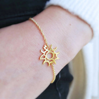 Zoom up on model's wrist with gold sun motif bracelet.